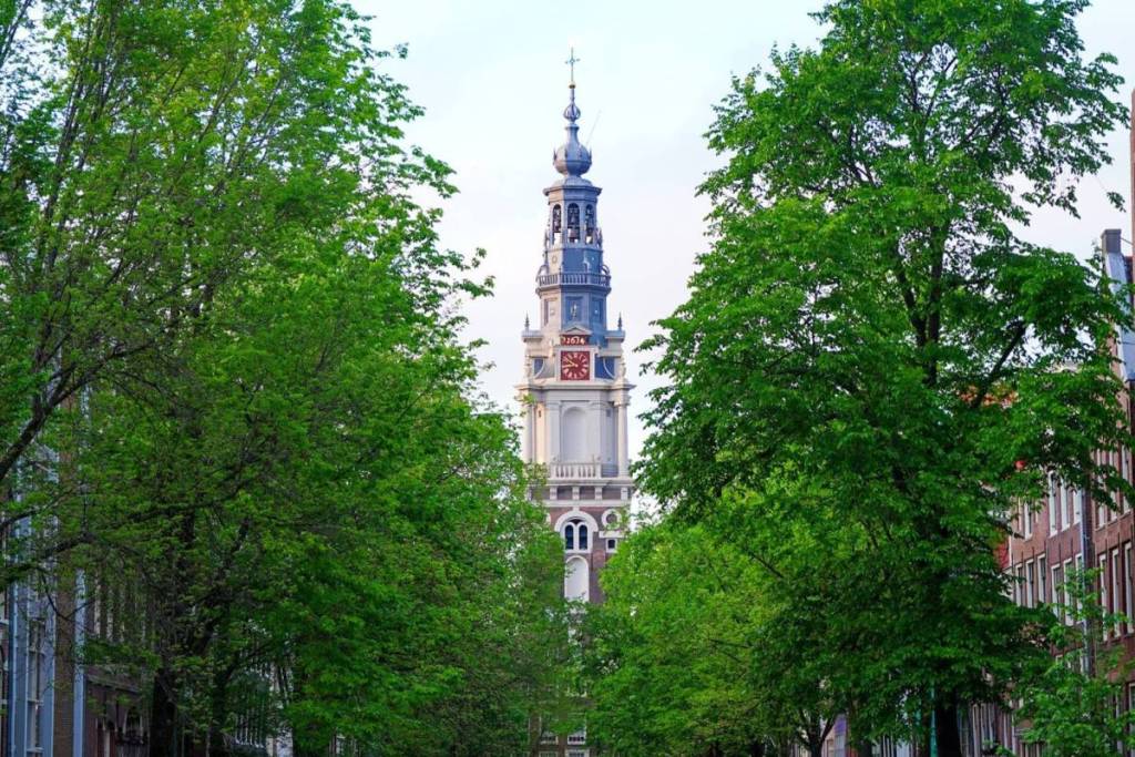 La clásica torre de la Zuiderkerk de Ámsterdam, escondida entre árboles frondosos.