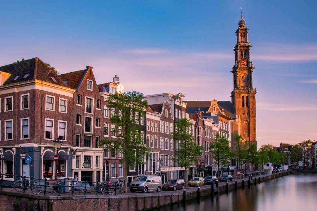 Vista del Prinsengracht con edificios históricos junto al canal y la torre de la Westerkerk en Ámsterdam al atardecer.