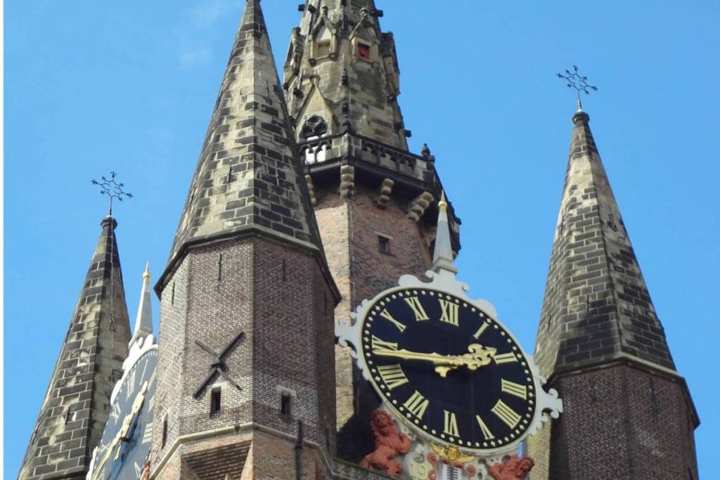 Primer plano de las agujas y el gran reloj de la Oude Kerk de Delft contra un cielo azul claro.