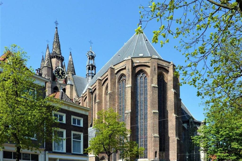 Vista de la iglesia gótica Oude Kerk de Delft, vista desde la calle entre la vegetación y los edificios históricos.