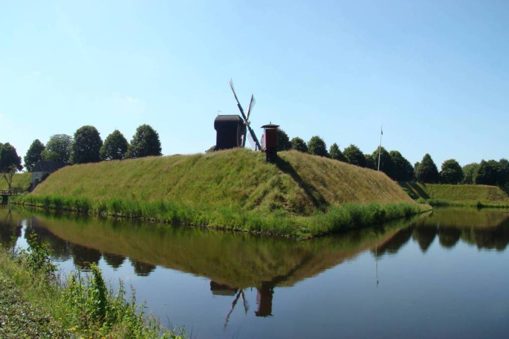 Un moulin à vent sur les remparts verdoyants de la forteresse de Bourtange, dont l’image se reflète dans l’eau calme du fossé.