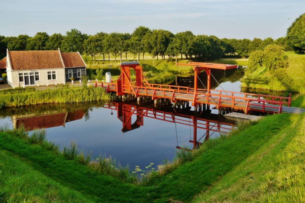 Un pont-levis en bois rouge qui attire l'œil enjambant les douves de la forteresse de Bourtange, avec un bâtiment historique en arrière-plan.