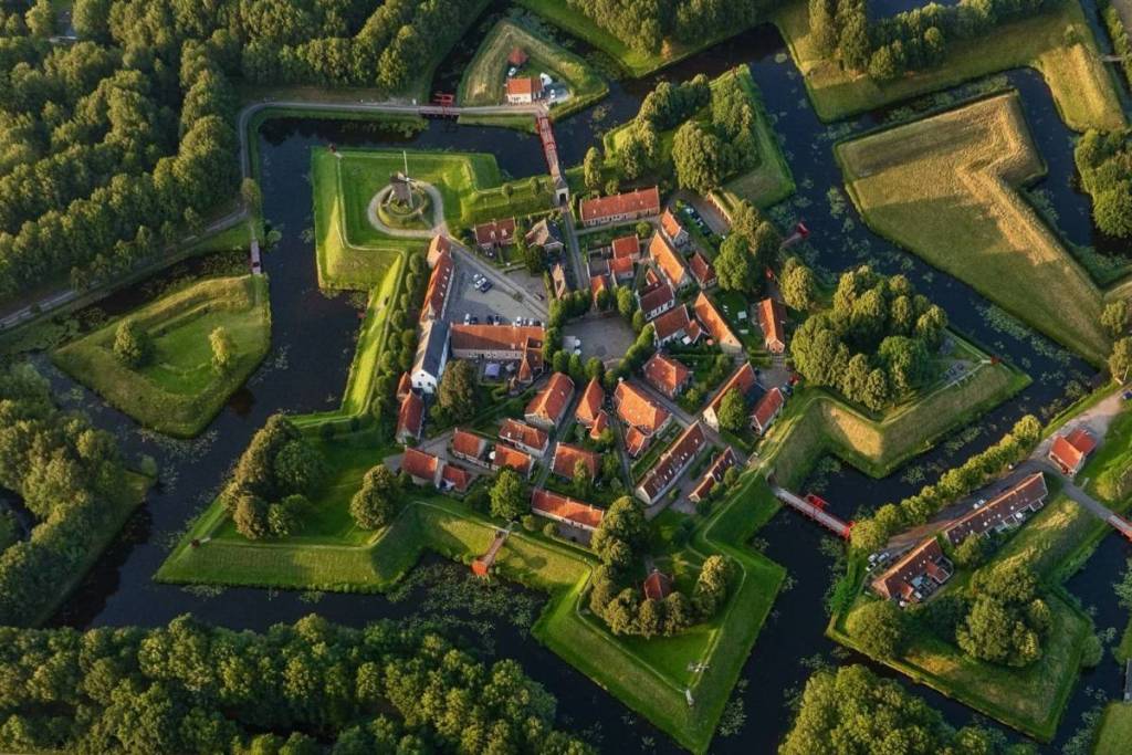 Photo aérienne en oblique de la forteresse en forme d'étoile de Bourtange, avec ses canaux caractéristiques, ses remparts verdoyants et les toits rouges du village.