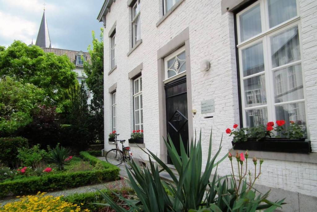 Gevel van een karakteristiek witgemaakt huis in Thorn met rode geraniums, een fiets voor de deur en een kerktoren op de achtergrond.
