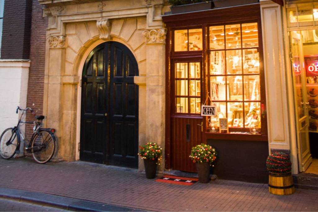 La casa más pequeña de Ámsterdam, en el número 22 de la Oude Hoogstraat, con el escaparate iluminado de la tienda de té, justo al lado de la puerta de la Iglesia Valona.