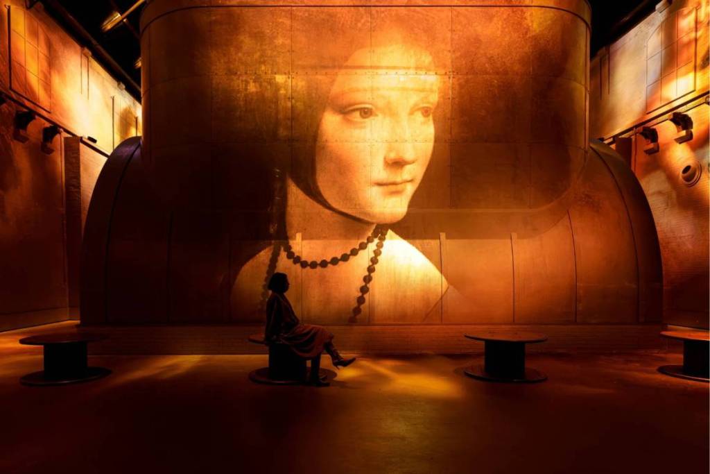Un visiteur dans la salle éclairée devant une grande projection immersive de « La Dame à l’hermine » de Léonard de Vinci à la Fabrique des Lumières d’Amsterdam.