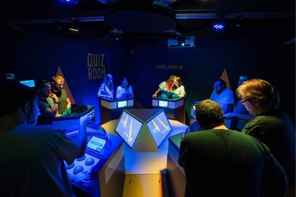 Dos equipos están concentrados en sus cabinas de quiz en el Quiz Room Middelburg, con una pantalla bien iluminada al fondo.