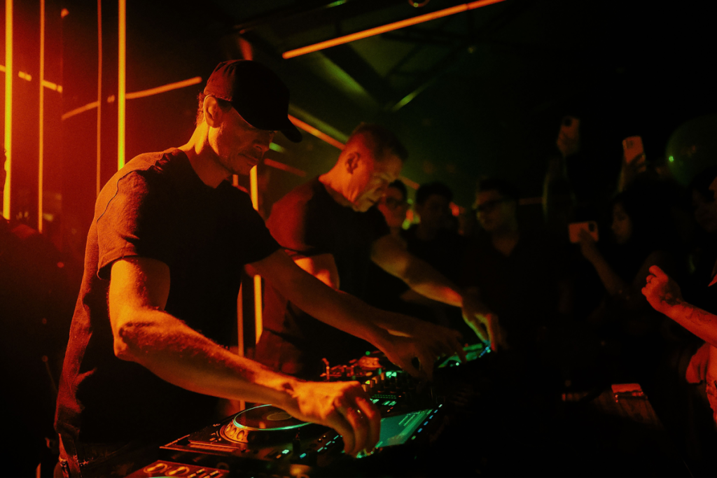 Een DJ achter de draaitafels in een sfeervol oranje verlichte Amsterdams nachtclub.