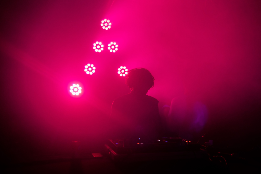 Silhouet van een DJ achter de mengtafel onder felroze podiumbelichting in een Amsterdamse club.