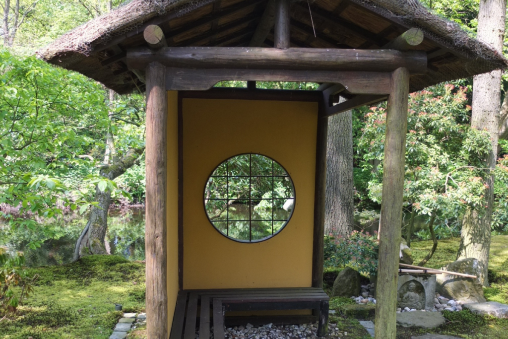 Traditioneller Teepavillon aus Holz mit einem runden Sichtfenster inmitten des grünen Moosteppichs im japanischen Garten des Landguts Clingendael.