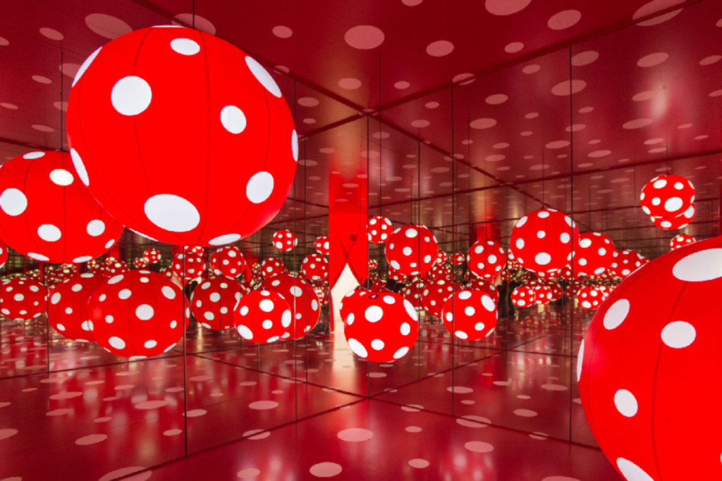 An immersive mirror room filled with glowing red inflatable balls covered in white polka dots, reflecting across the space.