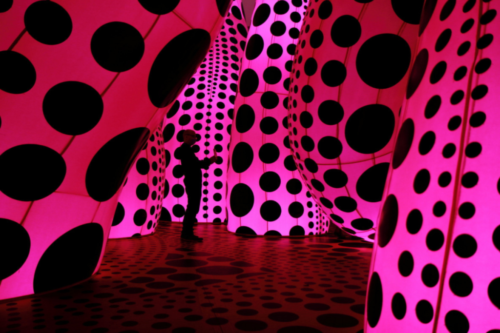 A visitor standing inside an installation room dominated by large pink tentacle-like structures covered in black polka dots.