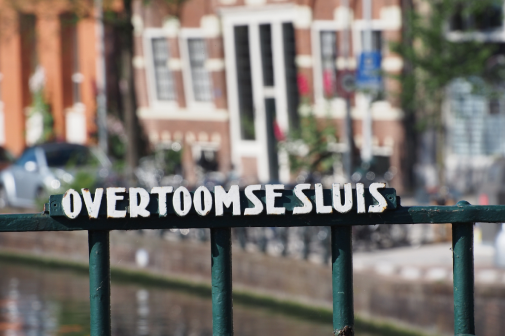 Das metallene Namensschild der Overtooms-Schleuse, angebracht an der grünen Brückengeländer in Amsterdam.