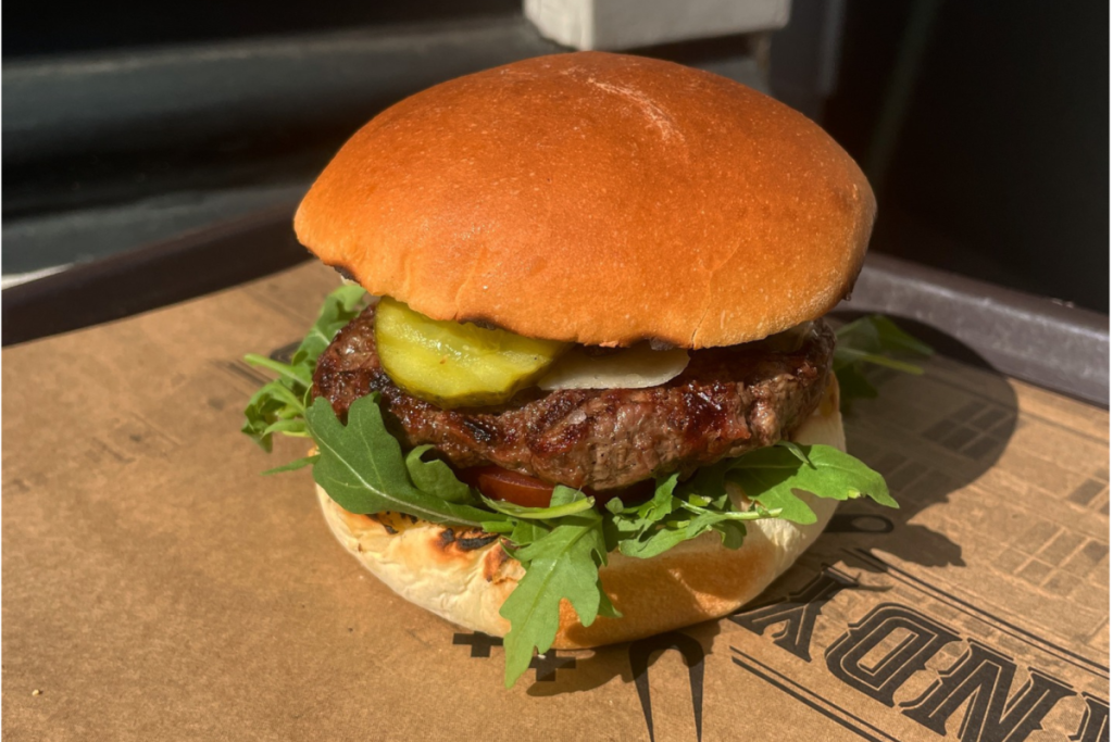 Dandy Burger in Amsterdam, serviert auf einem Brioche-Brötchen mit Rucola, Gewürzgurke und gegrilltem Rindfleisch.