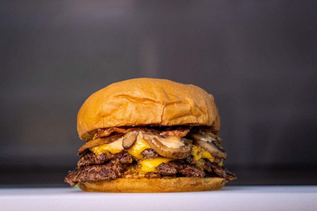 Smashburger mit geschmolzenem Cheddar, gebratenen Champignons, Speck und Haussauce in Amsterdam.