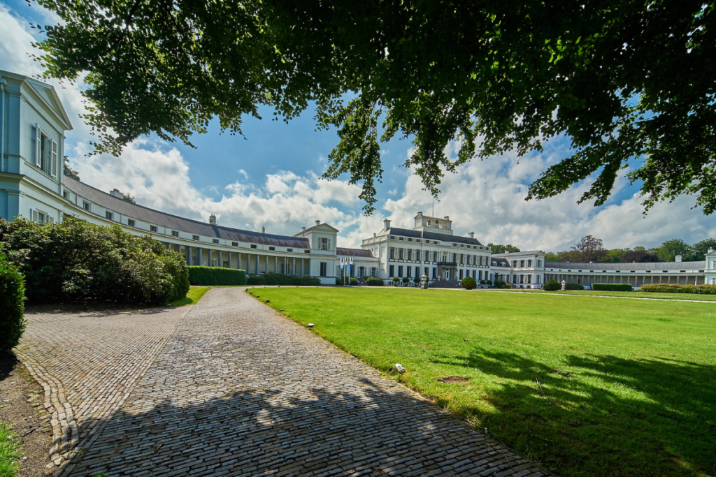 Blick auf die Vorderseite des Palasts Soestdijk mit den weißen Kolonnaden und dem großen Vorplatz.