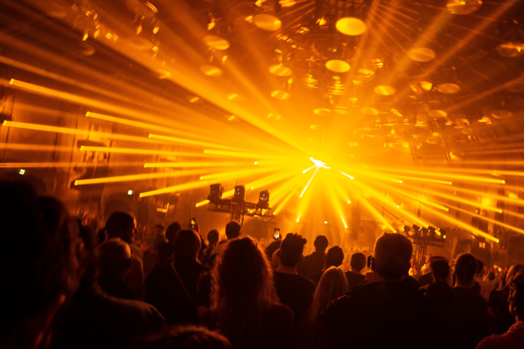 Stimmungsvolle Clubnacht während des Amsterdam Dance Event mit intensiven gelb-orangefarbenen Lasern, Lichtstrahlen und tanzendem Publikum.