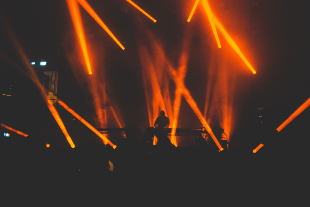 Silueta de un DJ detrás de la cabina, iluminada por intensos rayos de luz naranja y humo durante una fiesta en el Amsterdam Dance Event 2026.