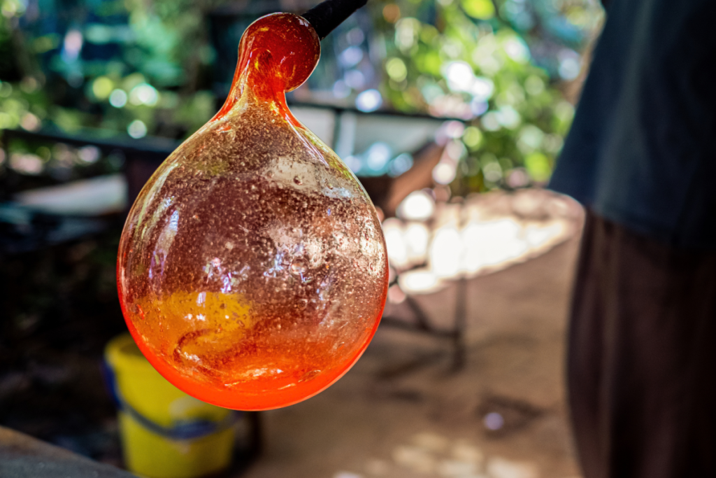 Ein Handwerker bläst bei einer Glasbläservorführung eine Kugel aus feurig-orangefarbenem, flüssigem Glas.
