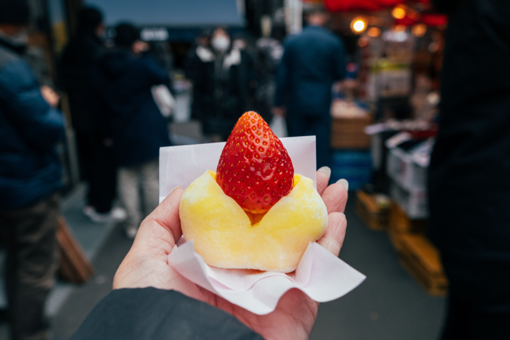 Eine Hand, die auf einem Markt ein traditionelles japanisches Ichigo-Daifuku-Mochi mit einer frischen Erdbeere hält.