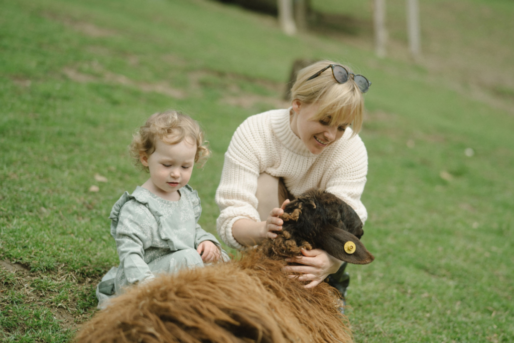 Eine Frau und ein kleines Kind, die gemeinsam auf dem Rasen eines Streichelzoos ein braunes Schaf streicheln.