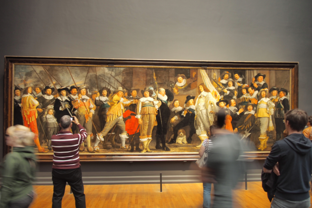 Besucher betrachten das große historische Gemälde „Die Nachtwache“ von Rembrandt van Rijn im Rijksmuseum.