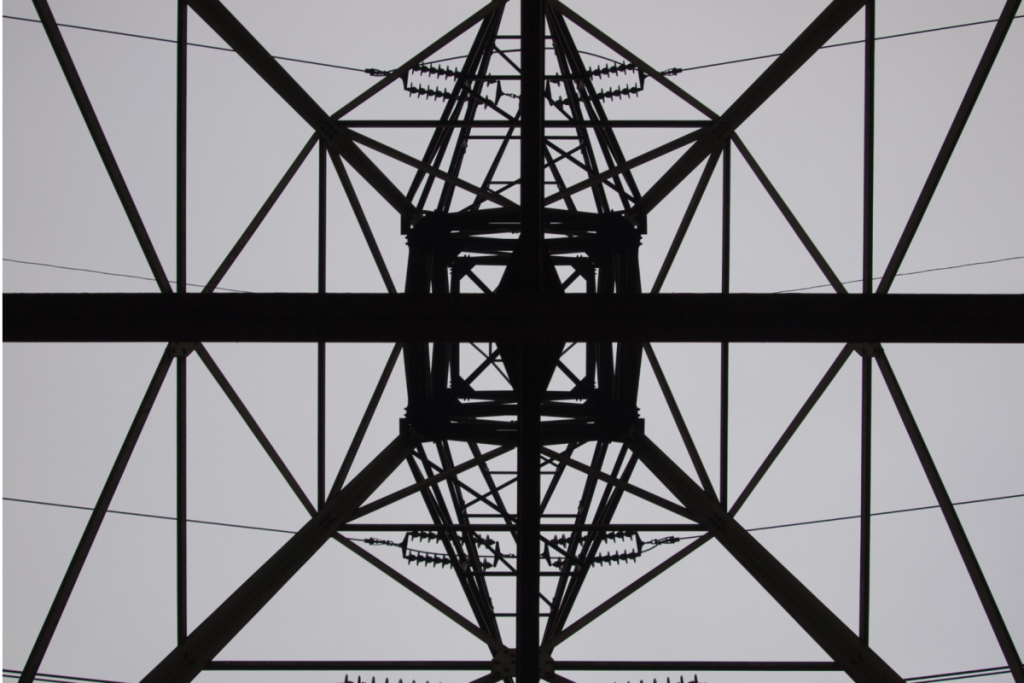 Untersicht eines Hochspannungsmasts aus Stahl mit komplexer Fachwerkkonstruktion vor grauem Himmel
