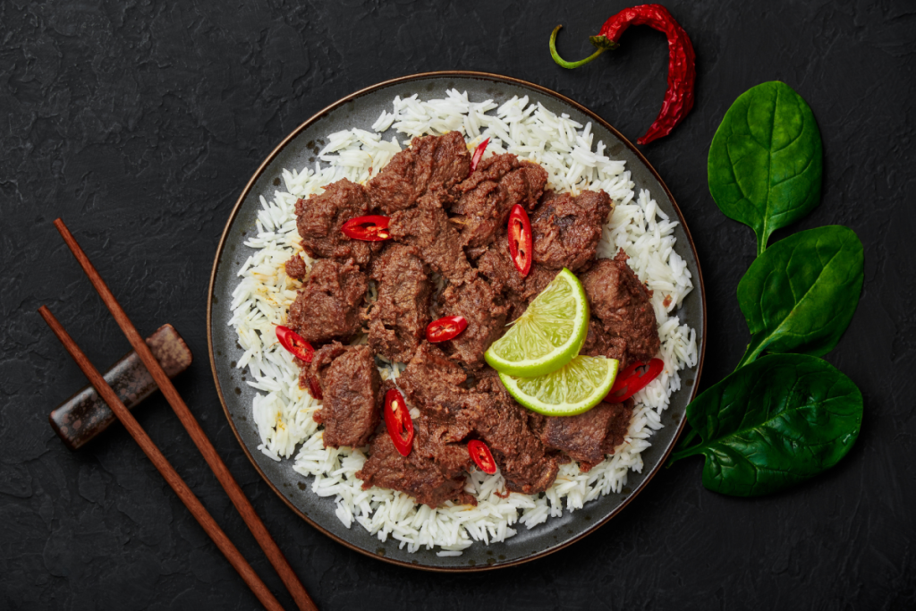 Eine Platte mit zartem indonesischem Rindfleisch-Rendang, serviert auf einem Bett aus weißem Reis mit frischer roter Chilischote und Limette