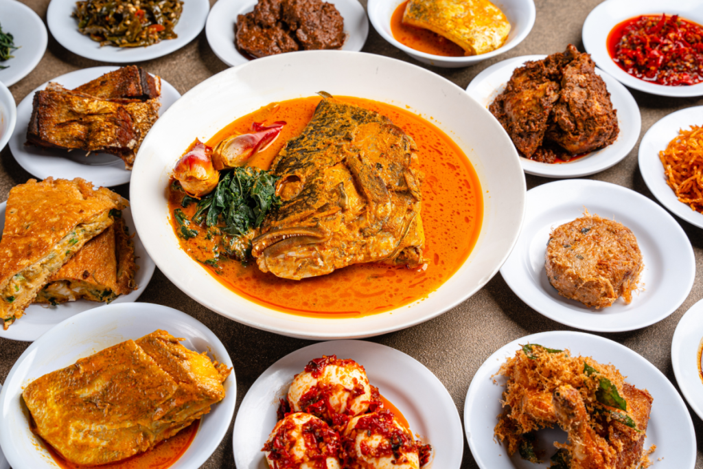 Ein reich gedeckter Tisch voller authentischer Padang-Gerichte aus der indonesischen Küche mit Gulai Kepala Ikan, Eiern in Sambal und Rendang.