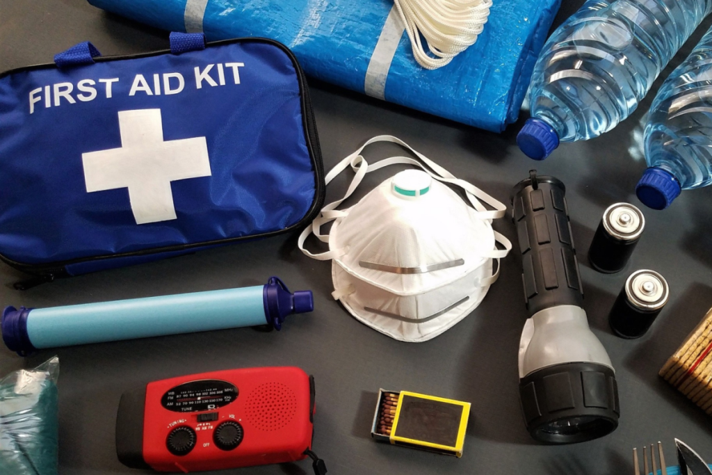 Inhalt eines 72-Stunden-Notfallpakets mit Erste-Hilfe-Tasche, Notfunkgerät, Taschenlampe, Streichhölzern und Trinkwasserflaschen für Notfälle.