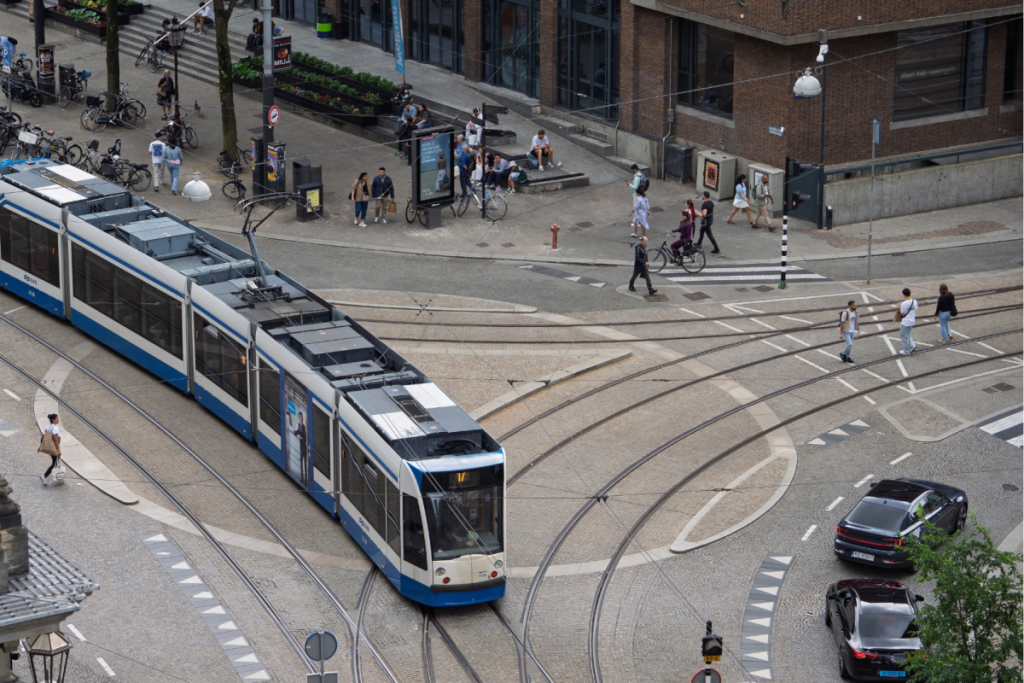 Draufsicht auf eine blau-weiße GVB-Straßenbahn, die über eine Kreuzung mit Straßenbahnschienen im Zentrum von Amsterdam fährt.