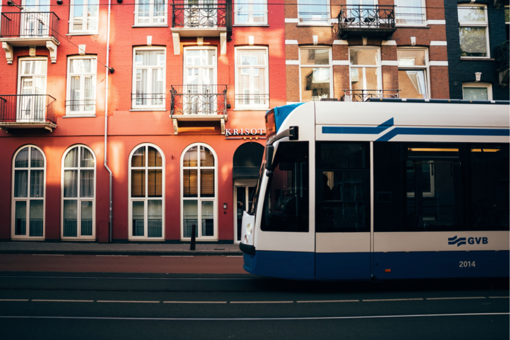 Seitenansicht einer modernen GVB-Straßenbahn, die an den charakteristischen roten Amsterdamer Gebäuden vorbeifährt.