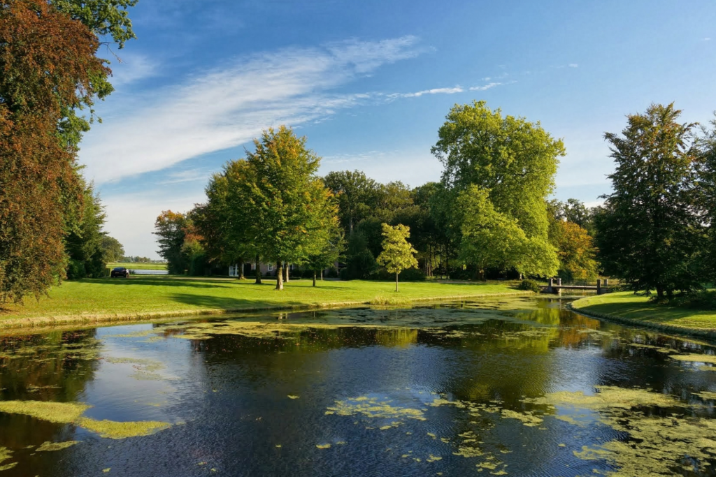 Der historische Schlossteich und die grünen Gärten von Schloss Duivenvoorde an einem sonnigen Sommertag.