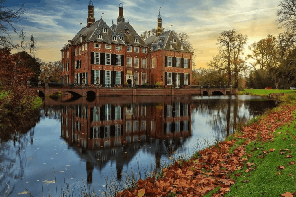 Schloss Duivenvoorde bei Sonnenuntergang mit Spiegelung im Wassergraben und Herbstblättern auf dem Rasen.