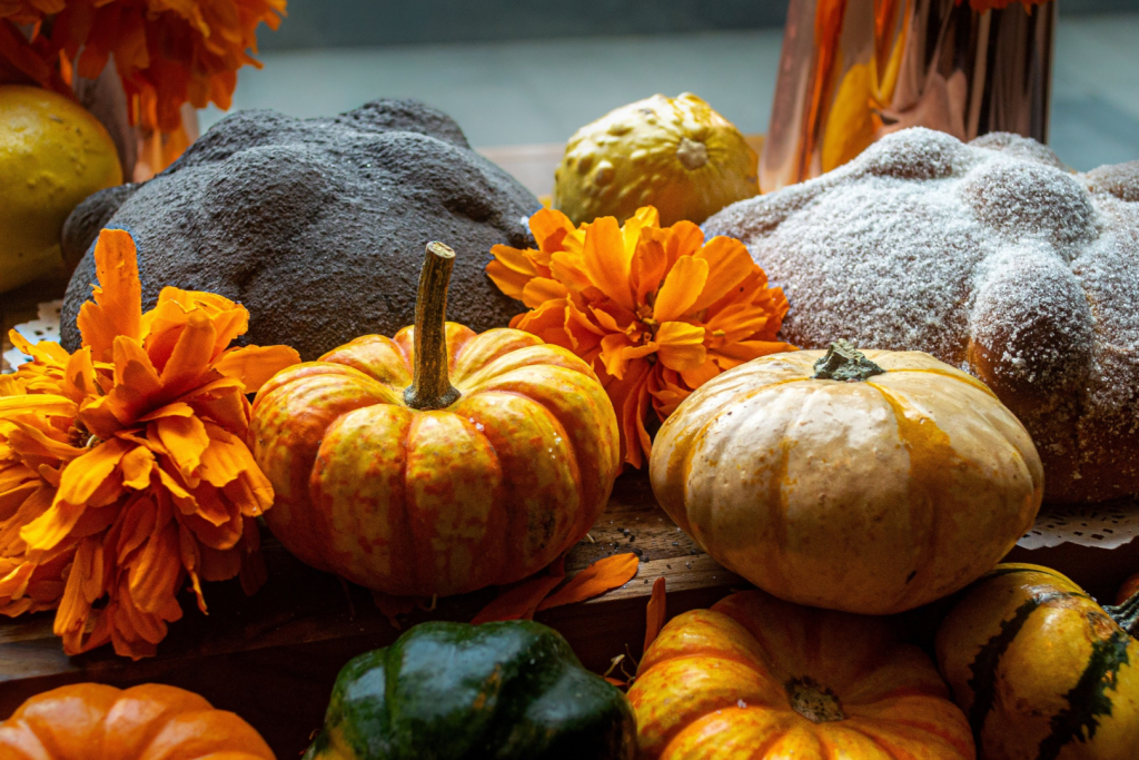 Frische Kürbisse, orangefarbene Blumen und handwerklich gebackenes Brot auf einem Holztisch