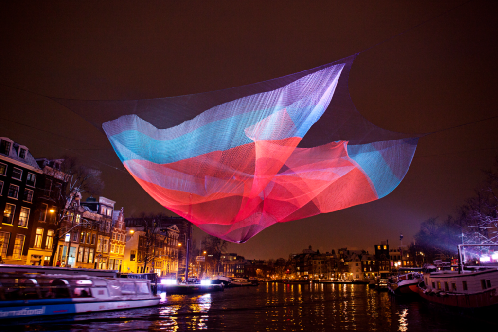 Farbenfrohes, schwebendes Netzkunstwerk von Janet Echelman über der Amstel während des Amsterdam Light Festivals.
