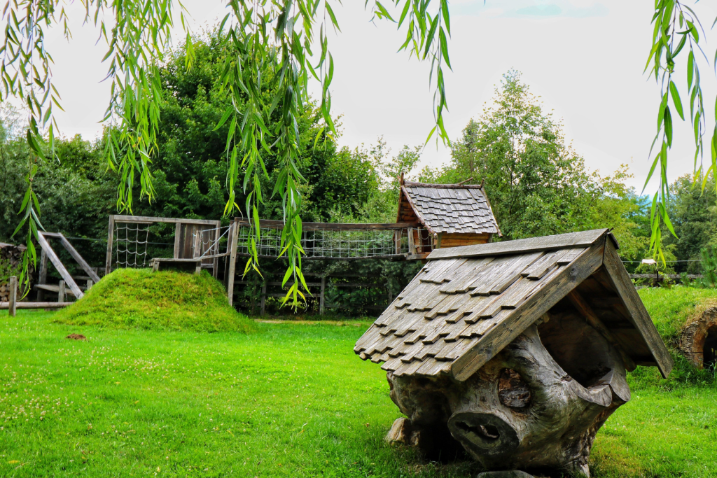 Holzspielhaus und Kletterparcours in einem grünen Naturspielplatz