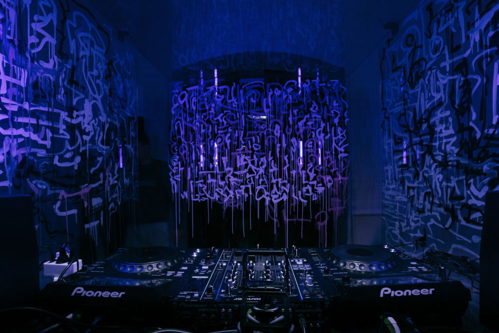 DJ-Equipment in einem dunklen Raum mit blauer und violetter Neonbeleuchtung und künstlerischen Wandmalereien