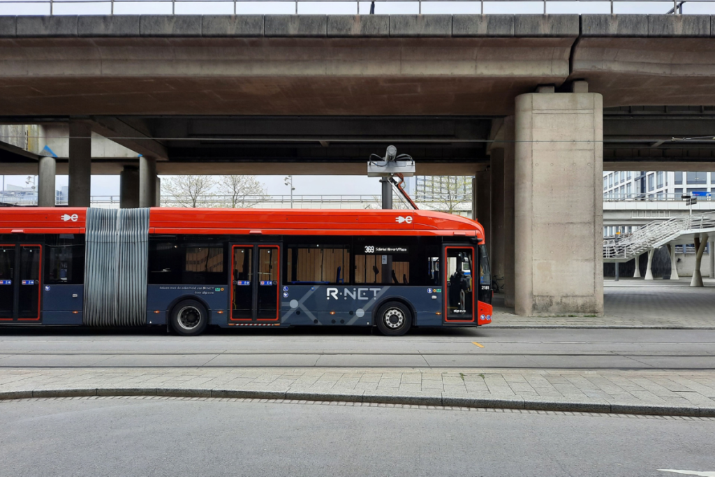 Ein roter Gelenkbus von R-NET steht an einer Bushaltestelle unter einer Überführung.