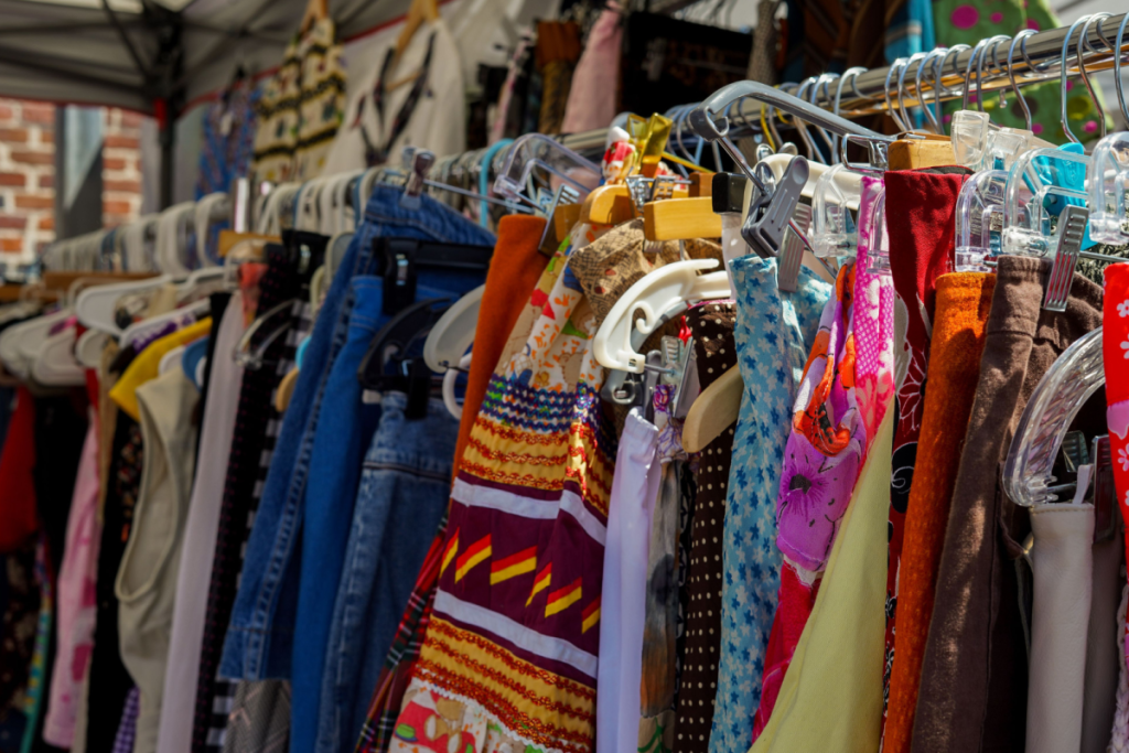 Farbenfrohe Secondhand-Kleidung und Vintage-Kleider auf Kleiderbügeln an einem Ständer auf einem Markt