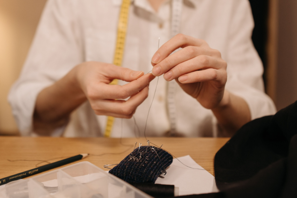 Nahaufnahme eines Schneiders, der in einem Atelier eine Nadel für eine Kleiderreparatur einstechen lässt