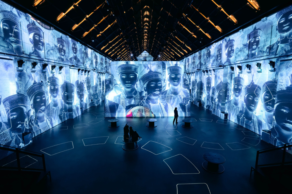 Blau beleuchteter Ausstellungsraum in der Fabrique des Lumières mit monochromen Porträts von Frauen in traditioneller Tracht von Jimmy Nelson.