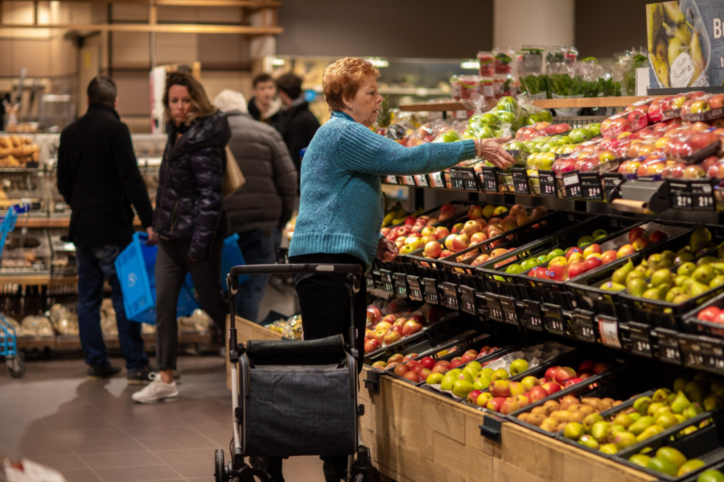 Eine Frau nimmt sich einen Apfel aus einer gut gefüllten Obst- und Gemüseabteilung mit frischem Angebot in einem gut besuchten Albert-Heijn-Laden.