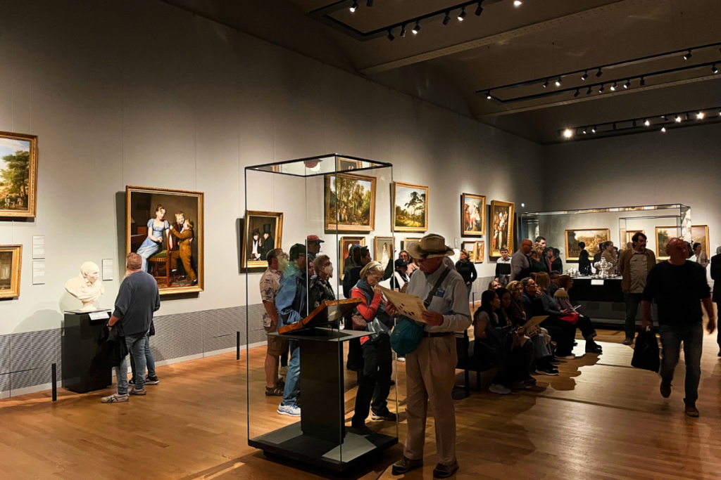 Besucher bewundern klassische Gemälde und Skulpturen in einem hell erleuchteten Ausstellungsraum des Rijksmuseums.