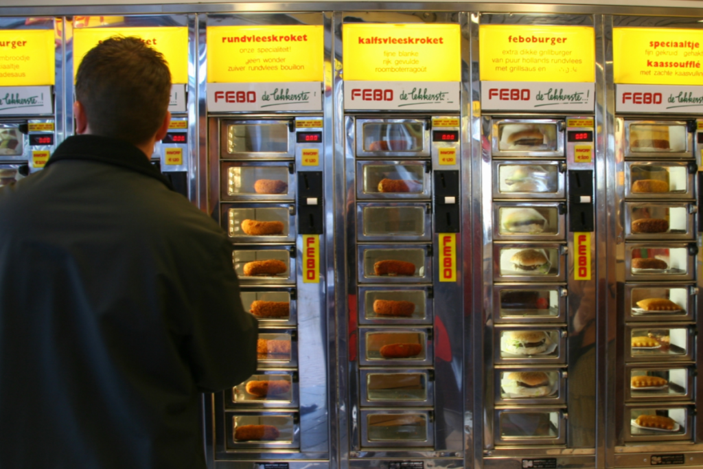 Ein Mann steht vor der beleuchteten Snackwand von FEBO, um sich eine warme Krokette aus der Wand zu holen.