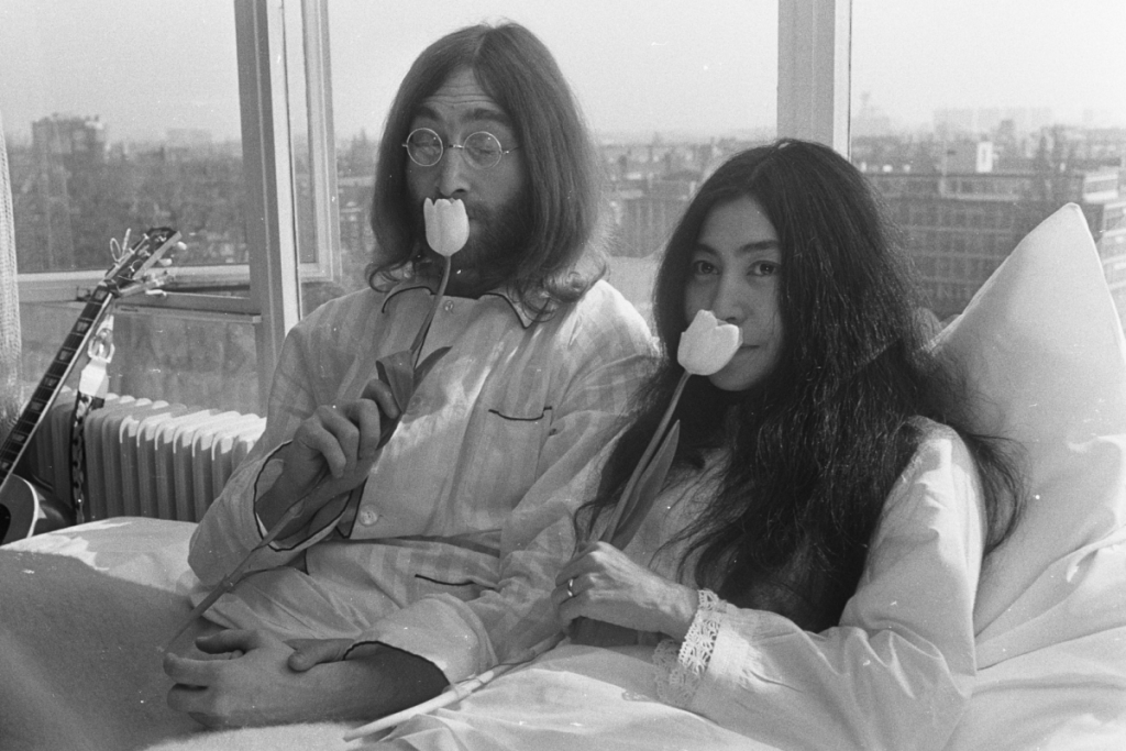 Nahaufnahme von John Lennon und Yoko Ono im Pyjama auf dem Bett in der Amsterdamer Hilton-Suite, während sie beide eine weiße Tulpe in der Hand halten.