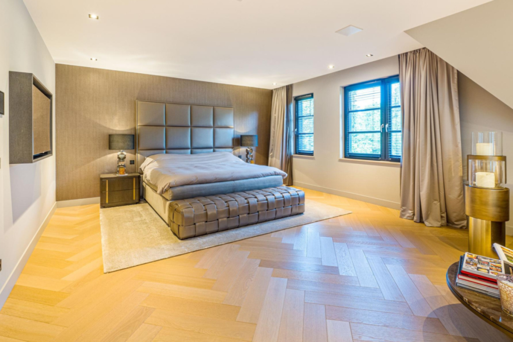 Master bedroom met een houten visgraatvloer, luxe hoofdbord en grote raampartijen met donkere kozijnen.