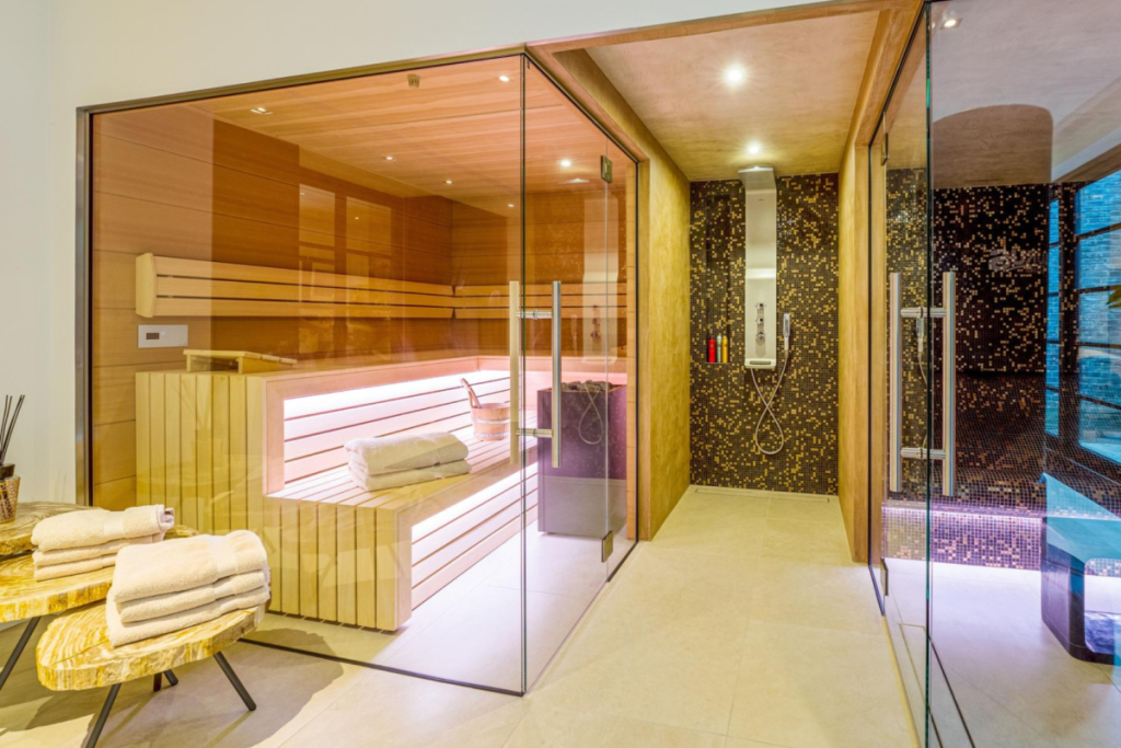 Luxe wellnessruimte in het souterrain met houten sauna, glazen wanden en inloopdouche met mozaïektegels.
