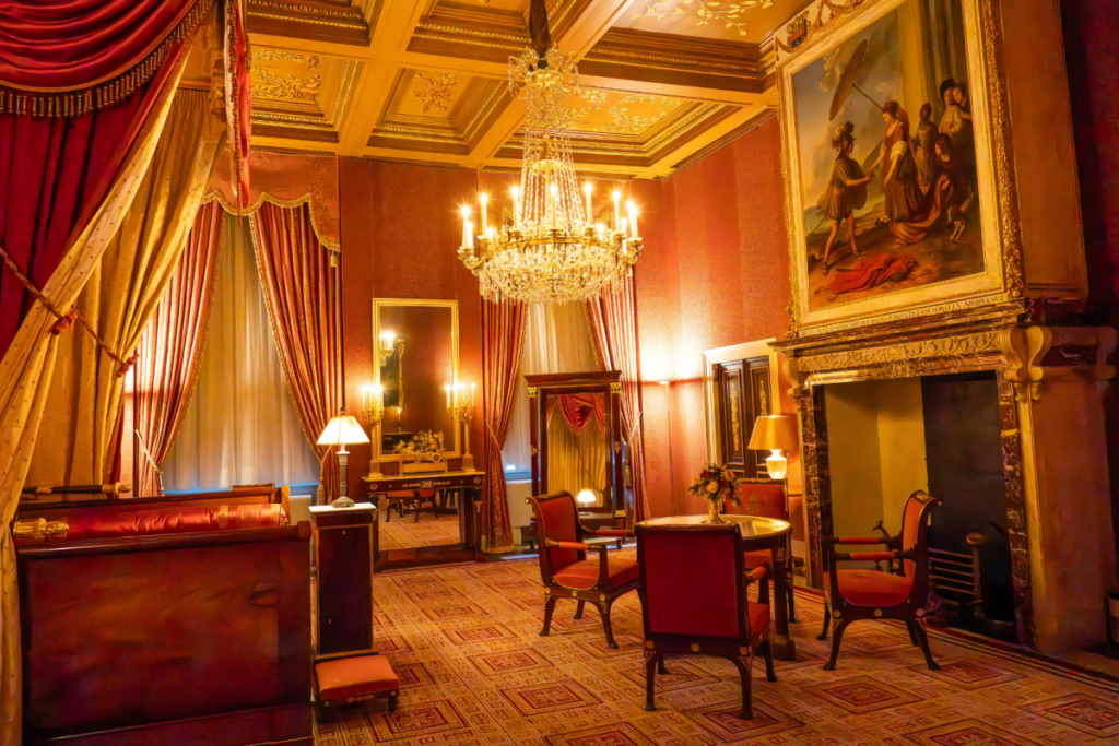 Historisch koninklijk vertrek in het Koninklijk Paleis Amsterdam met rood empire-meubilair, kristallen kroonluchter en klassieke schouw