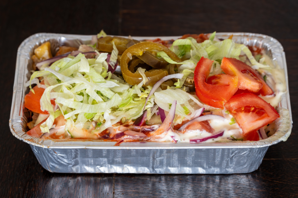 Bovenaanzicht van een traditionele kapsalon in een aluminium meeneembak met friet, vlees, gesmolten kaas, ijsbergsla, tomaat en jalapeño's.